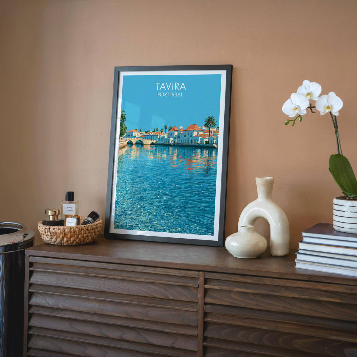 Tavira Portugal wall art, black frame on a walnut sideboard against a terracotta wall with a white orchid