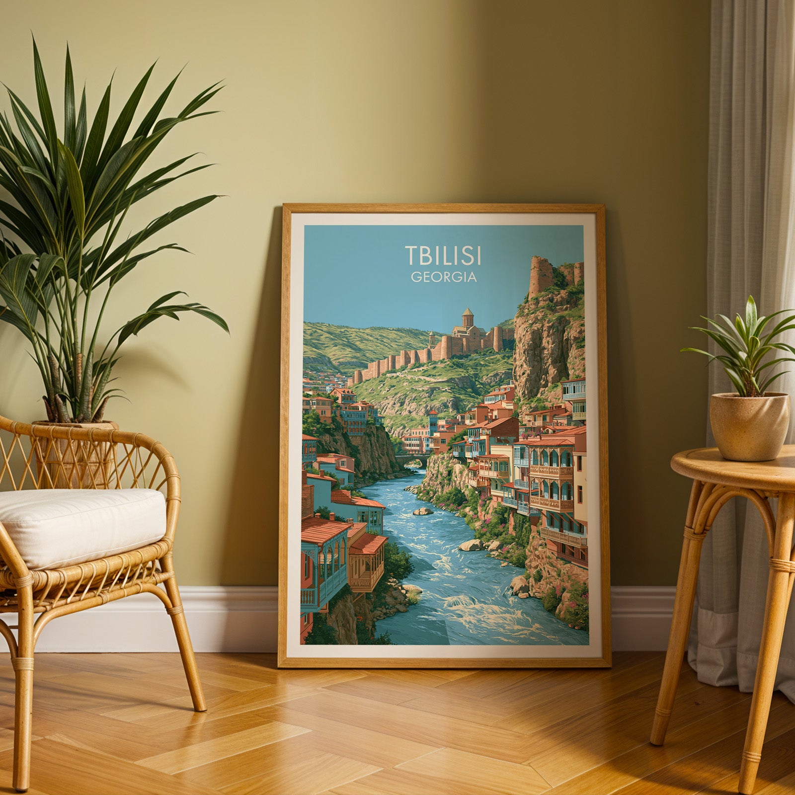 Large Tbilisi Georgia travel print in an oak frame leaning on a herringbone floor next to a rattan chair