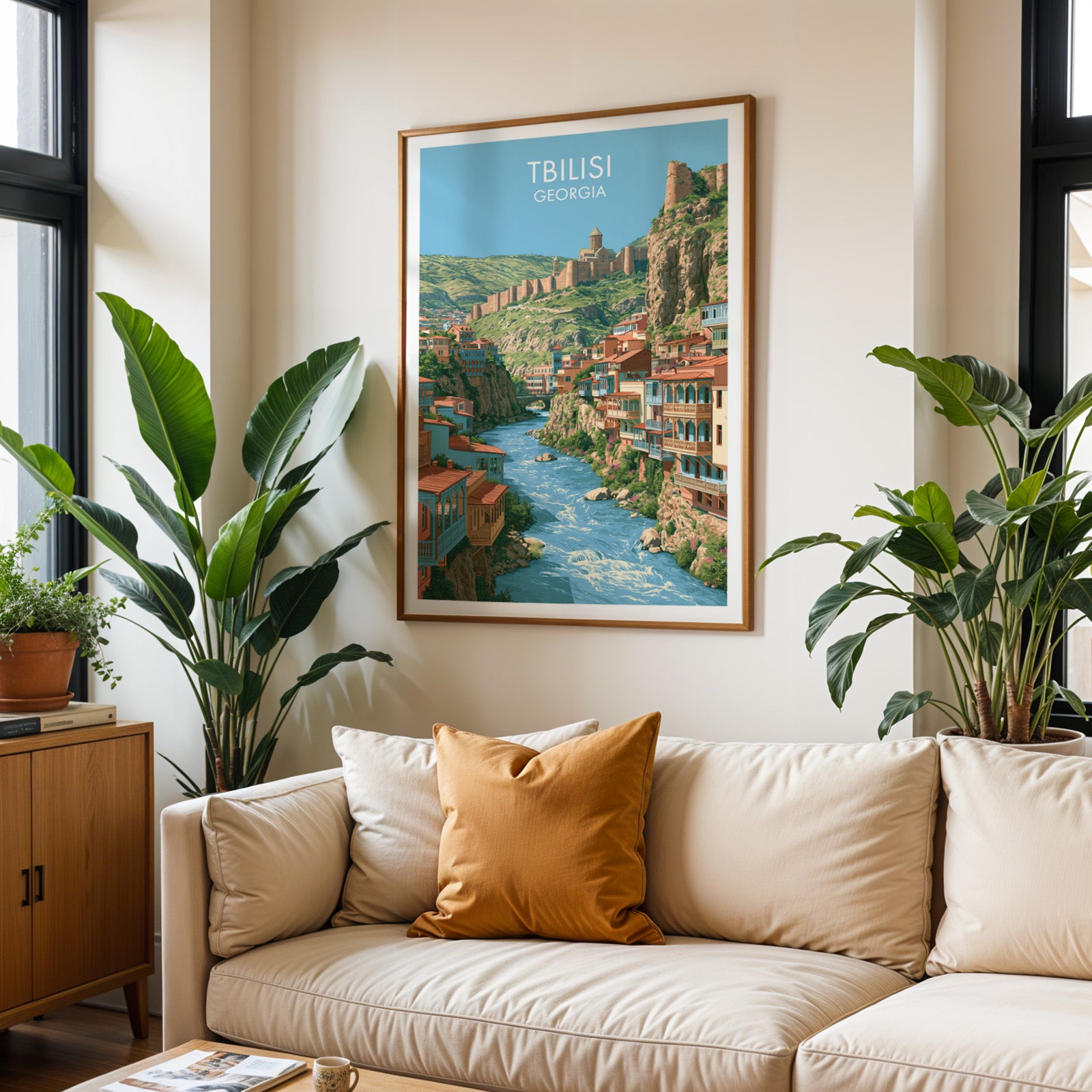 Framed Tbilisi Georgia wall art hanging above a cream sofa in a bright living room with tropical plants