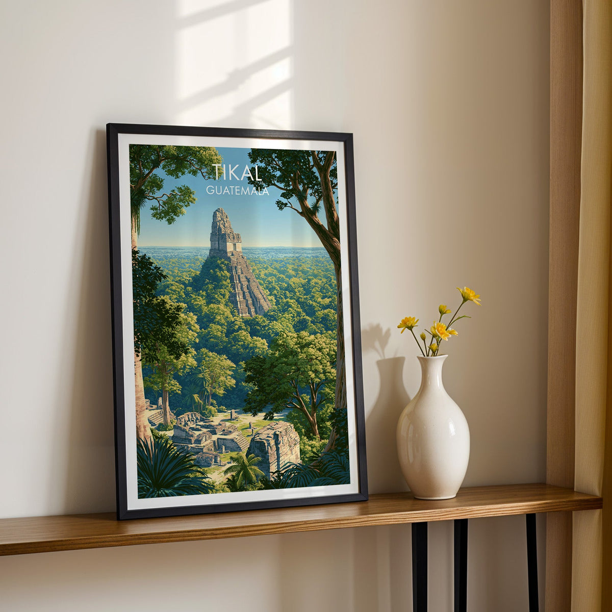 Maya temple roof comb in a black frame on a narrow wood shelf, yellow daisies against a sunlit cream wall