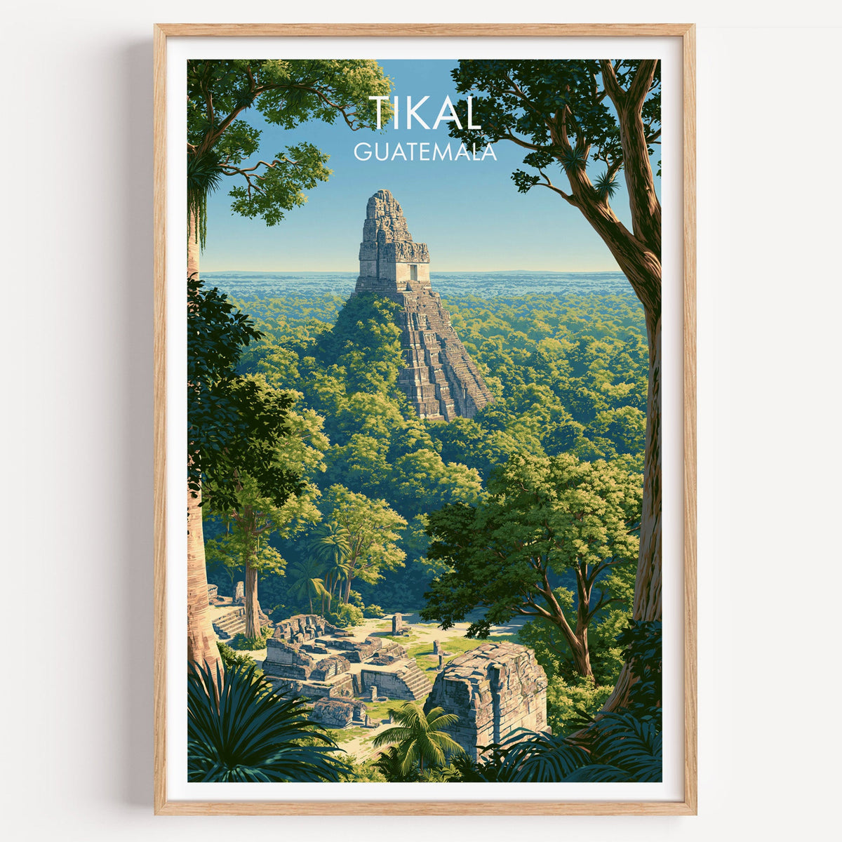 Tikal Guatemala travel print in a light oak frame on a plain white wall, stone temple above the treetops