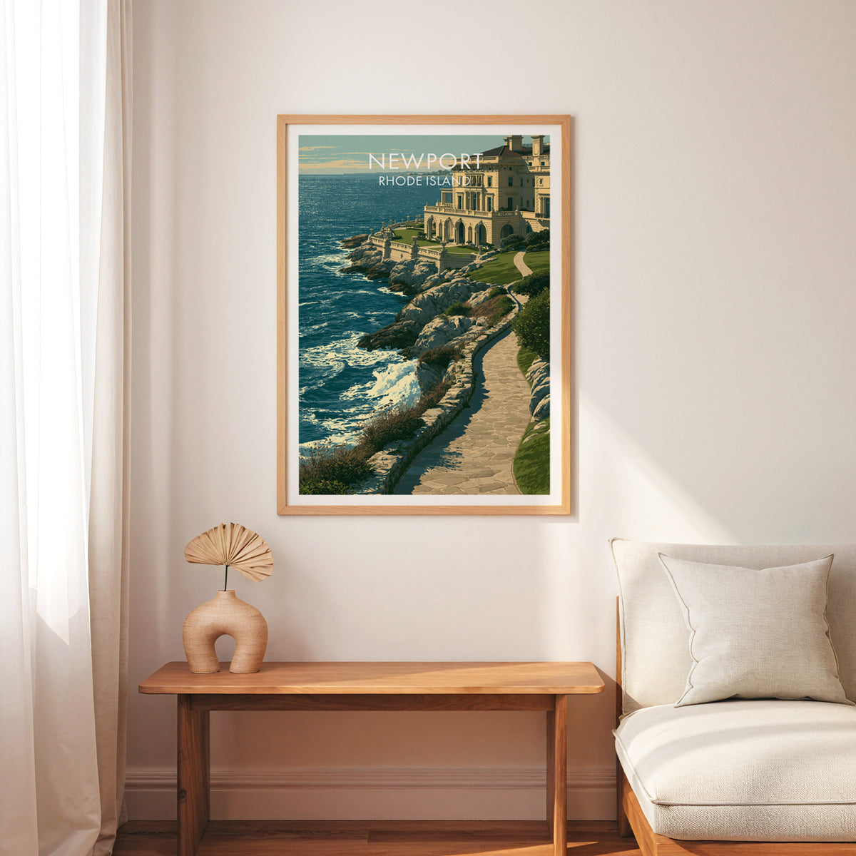Newport travel poster in an oak frame above a slim wood bench, cream armchair and a palm-leaf fan.