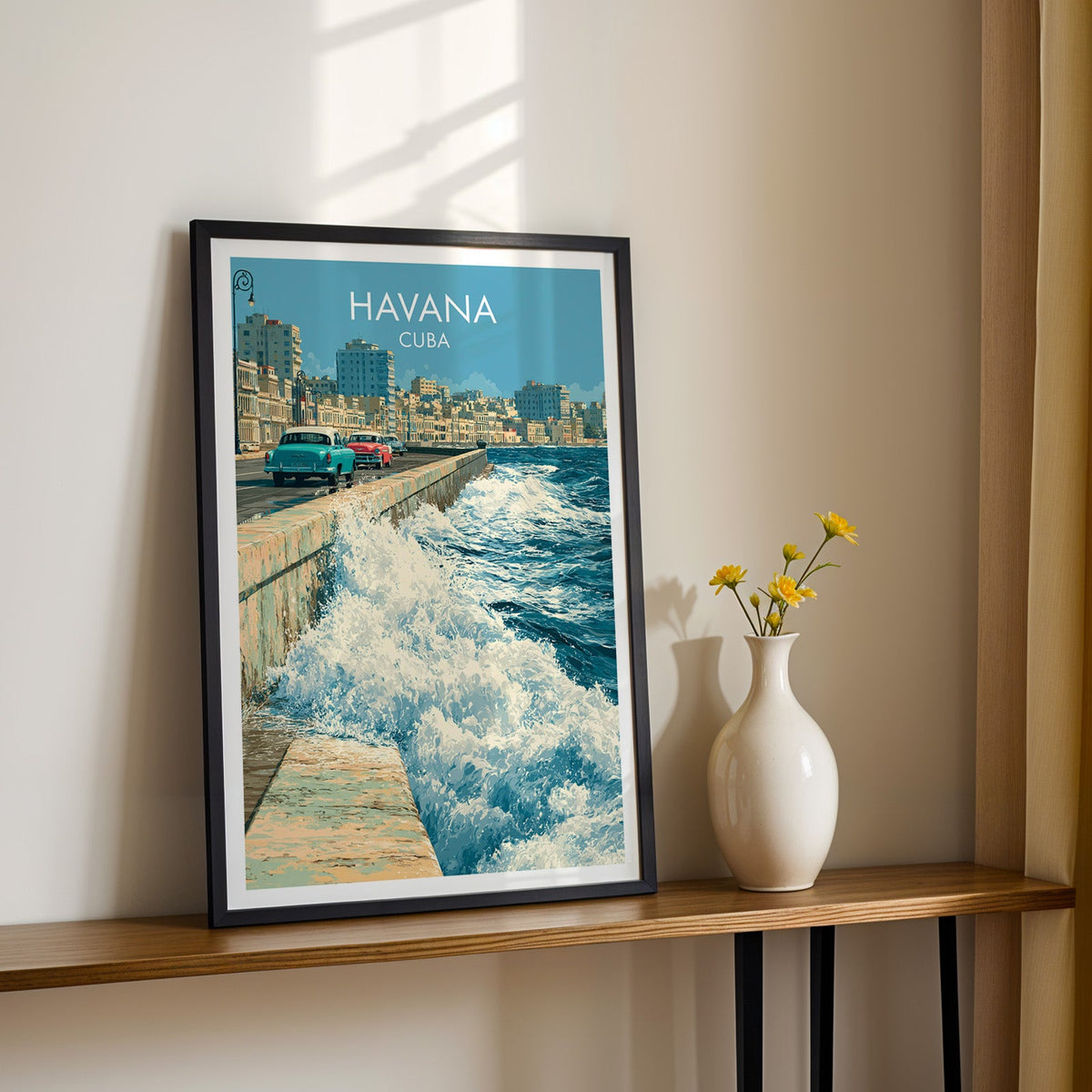 Sea spray over the Malecon in a black frame on a narrow wood shelf with yellow daisies against a sunlit cream wall