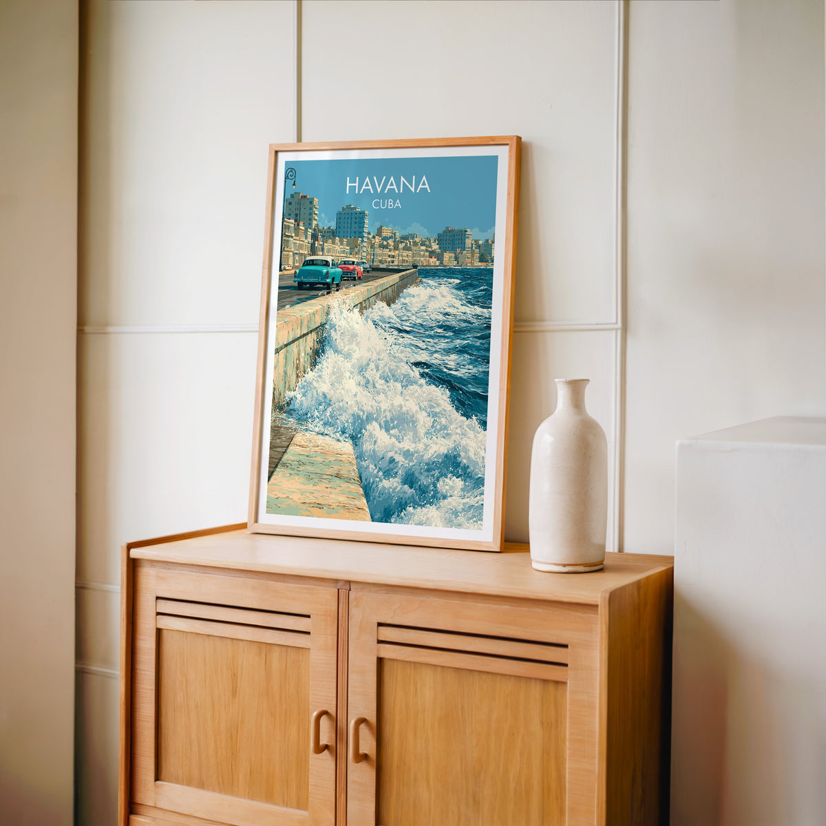 Havana skyline across the bay in an oak frame on a light oak cabinet, cream panelled wall, pale bottle vase right