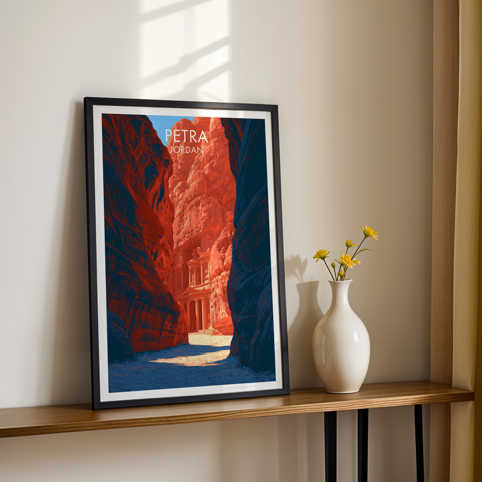 Black framed Petra Jordan Treasury print on a narrow hallway console in sunlight, styled with yellow flowers