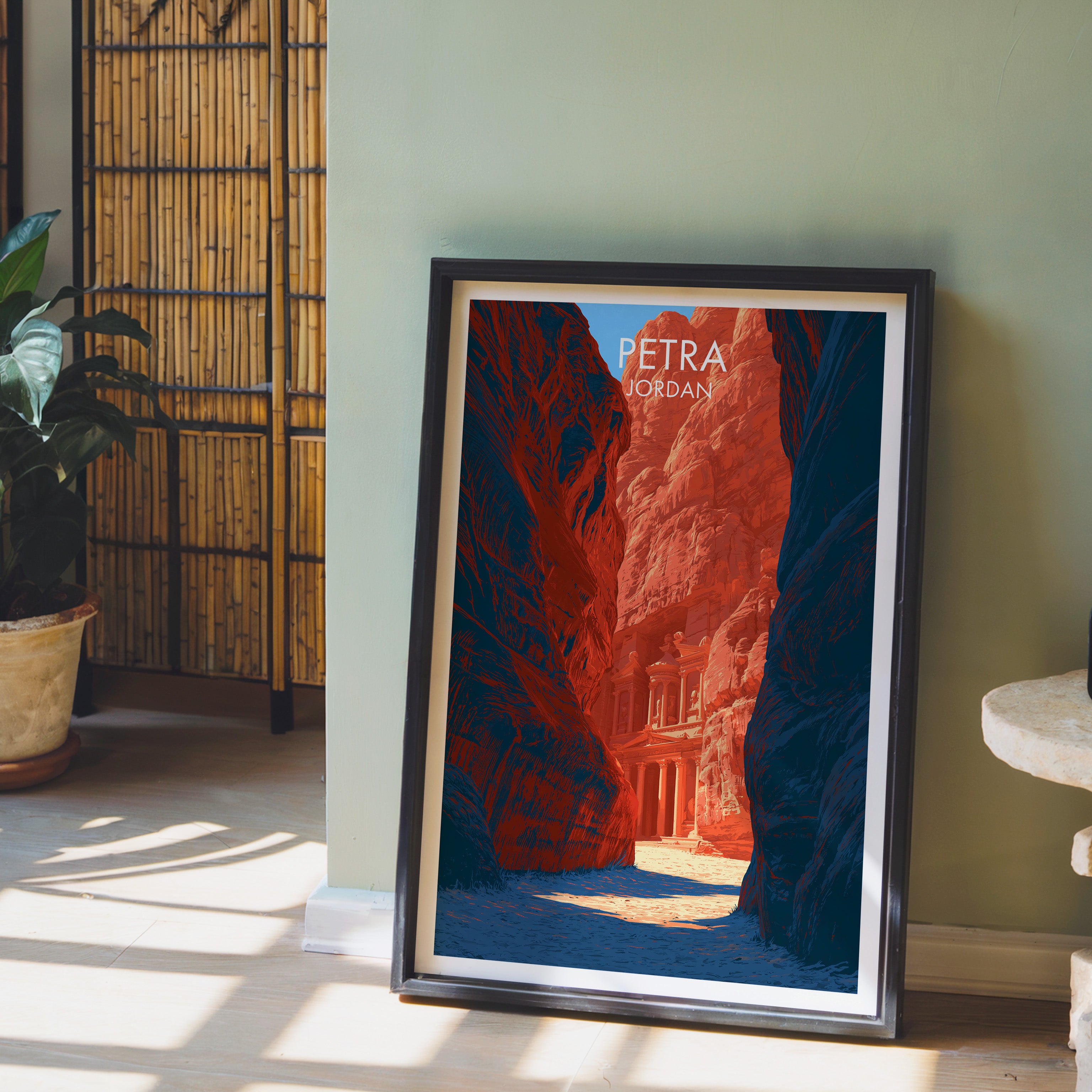 Petra Jordan Treasury wall art in a black frame leaning against a sage green wall beside a bamboo screen