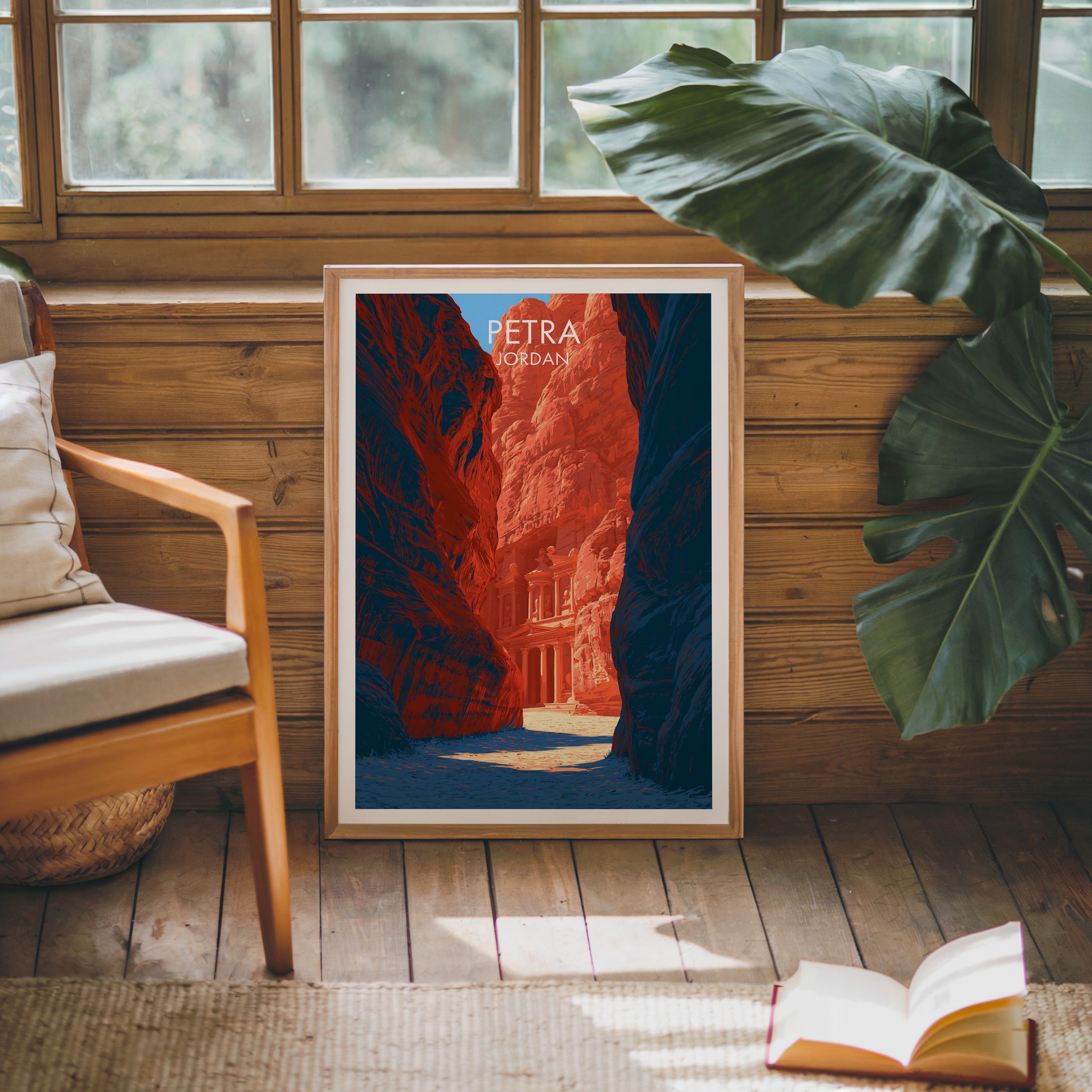 Framed Petra Jordan Treasury poster leaning against a timber cabin wall with monstera leaves and an open book