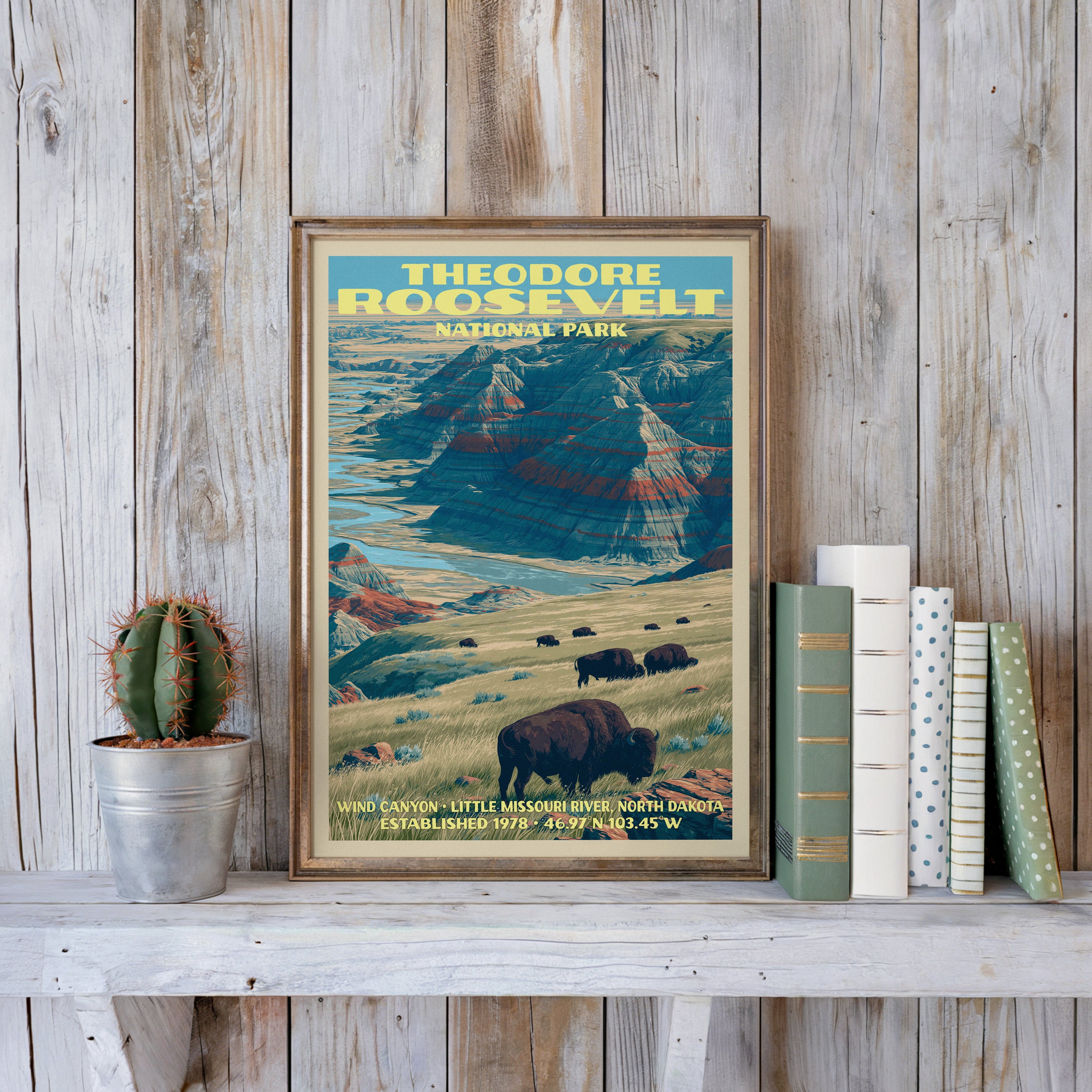 Wind Canyon badlands print in a slim gold frame on a whitewashed plank wall beside a cactus and books