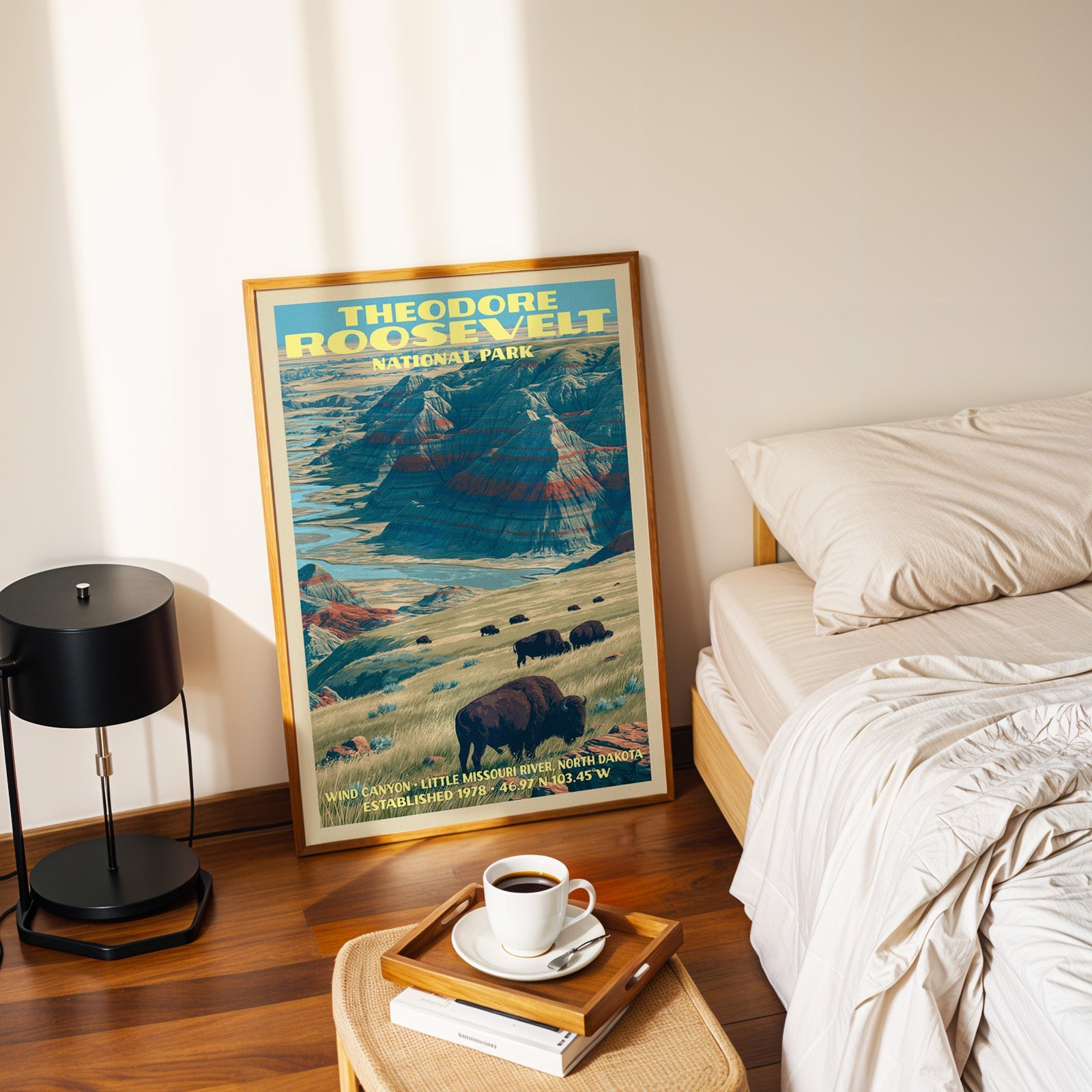 Wind Canyon Theodore Roosevelt print in a gold frame on the floor beside a made bed and a table lamp