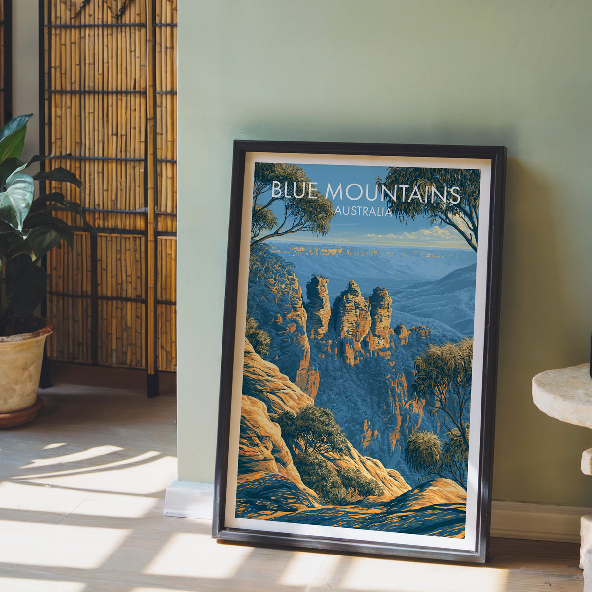 Three Sisters artwork in a black frame on pale wood floor by a sage-green wall and bamboo screen