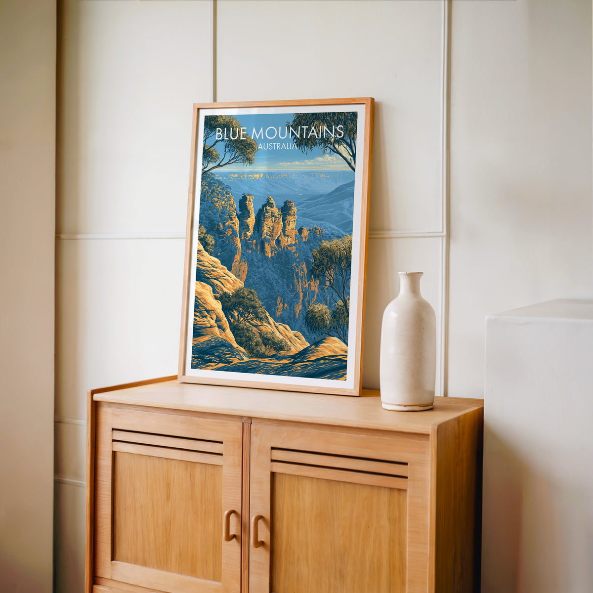 Three Sisters print in an oak frame on a light oak cabinet beside a pale bottle vase