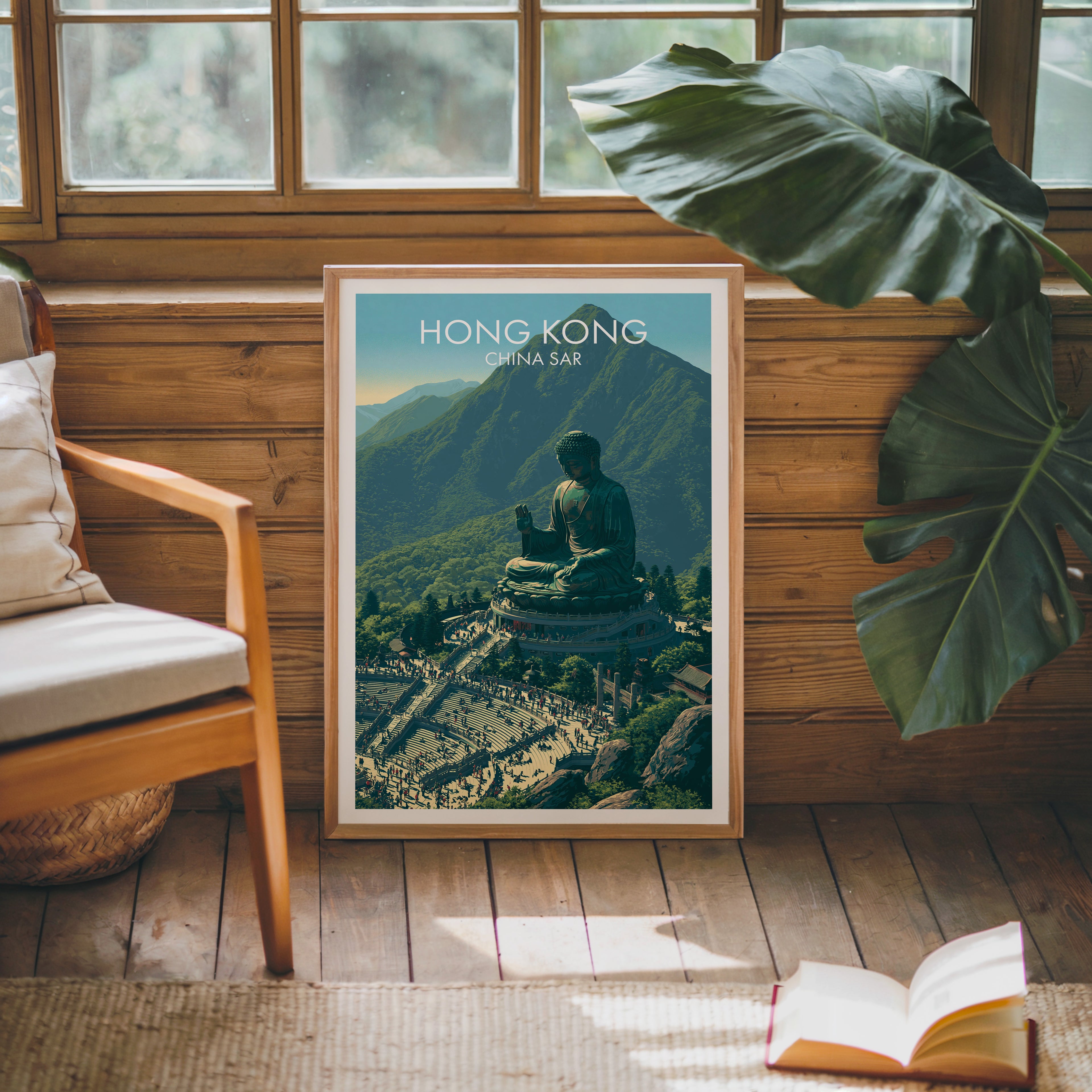 Framed Tian Tan Big Buddha Hong Kong poster leaning against a timber cabin wall with monstera leaves and an open book