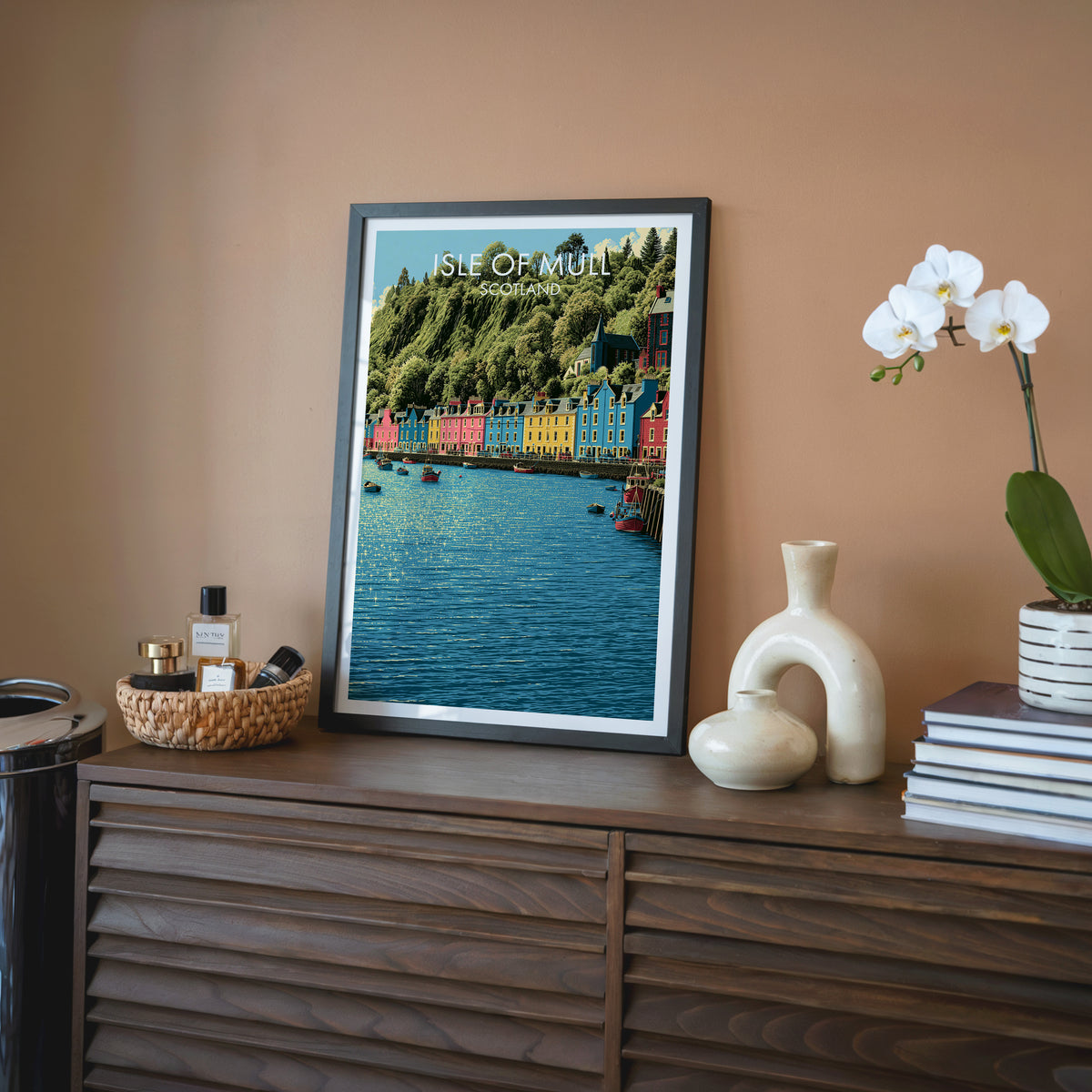 Tobermory Isle of Mull wall art, black frame on a walnut sideboard against a terracotta wall with a white orchid