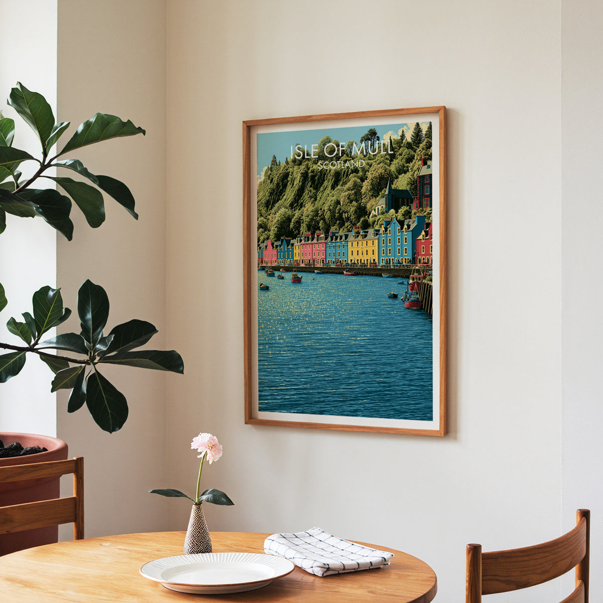 Tobermory waterfront poster, walnut frame in a dining corner above a round table and a fiddle-leaf fig