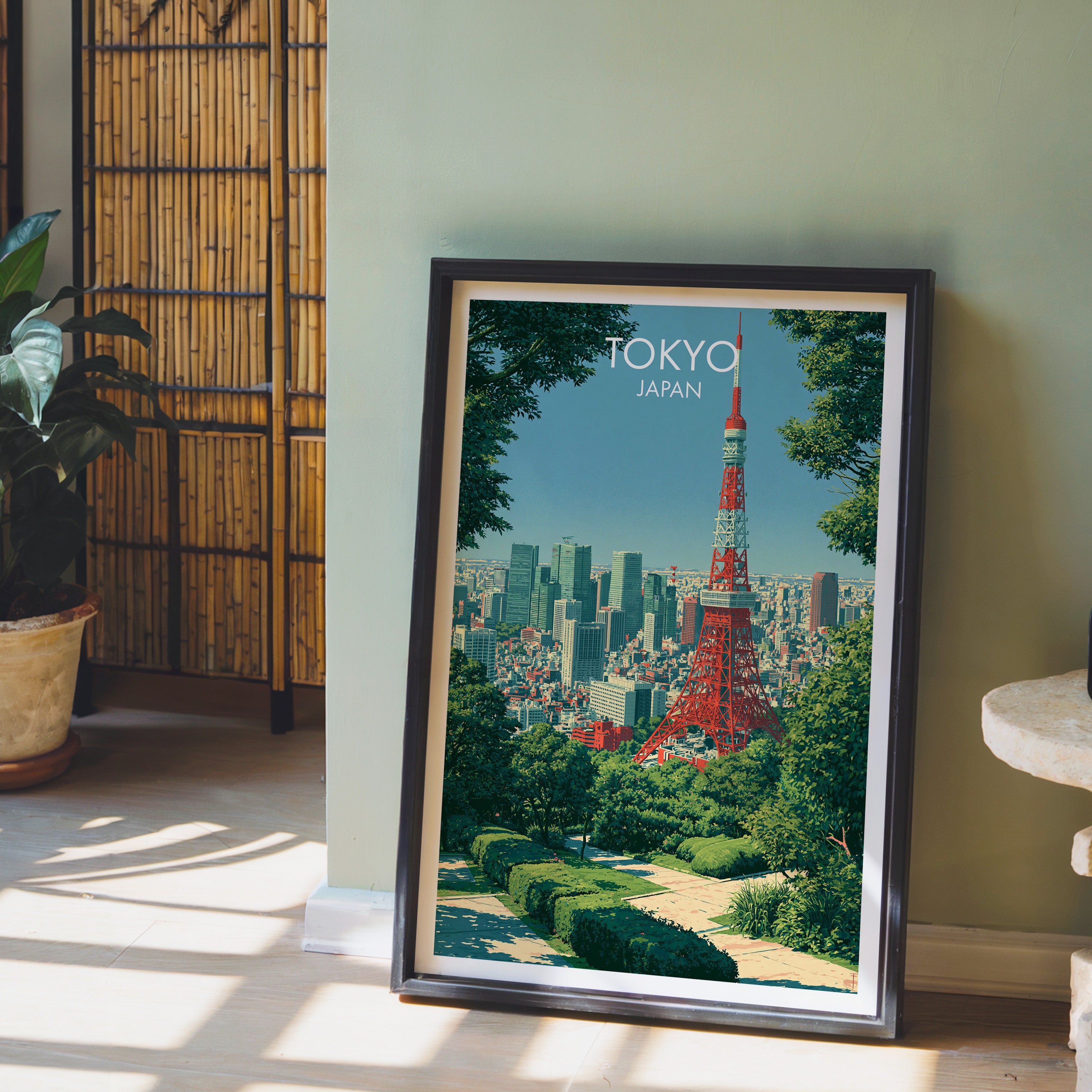 Tokyo Tower Japan wall art in a black frame leaning against a sage green wall beside a bamboo screen