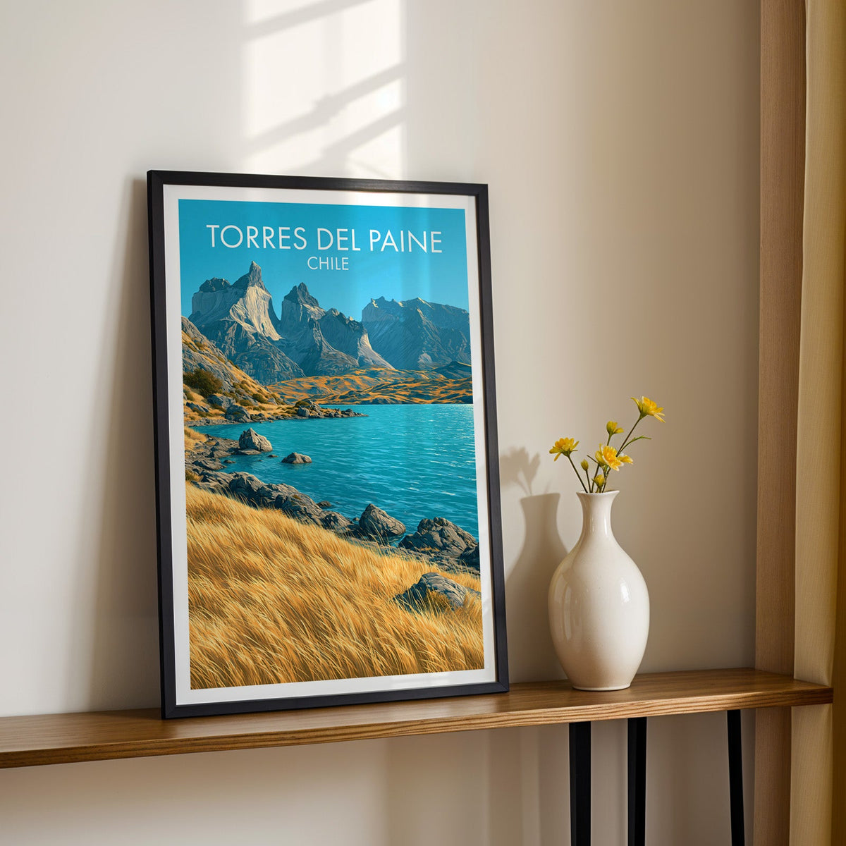 Cuernos del Paine wall art in a black frame on a narrow wood shelf with black iron legs and yellow daisies in sun