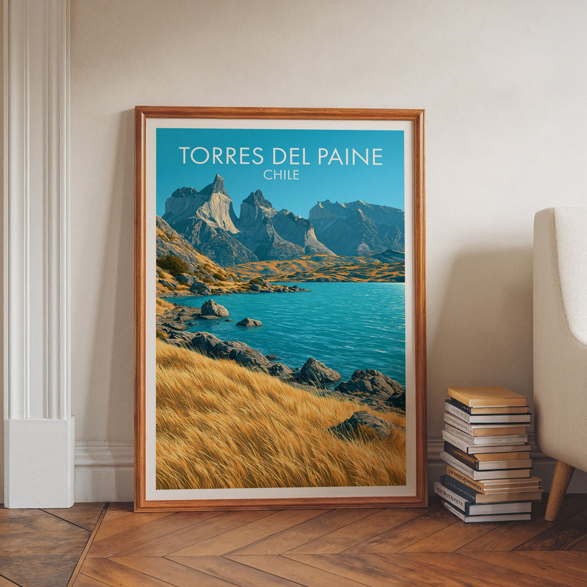 Torres del Paine travel print in a walnut frame on herringbone floor by white moulding, book stacks and a cream chair