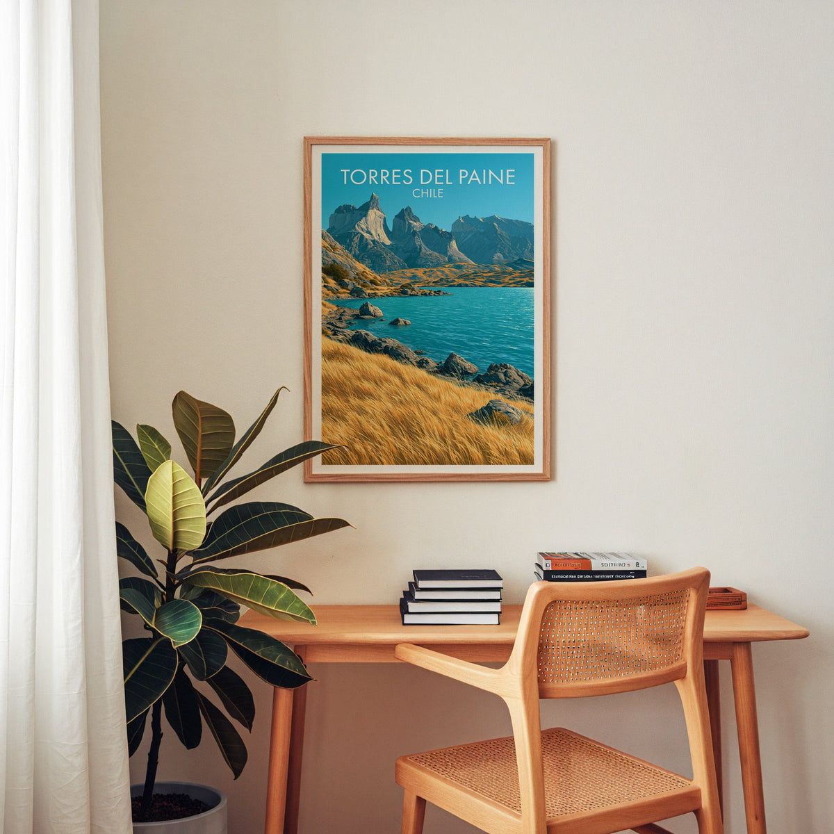 Chile mountain poster in an oak frame above a wood desk with cane chair, books and a rubber plant in a home office