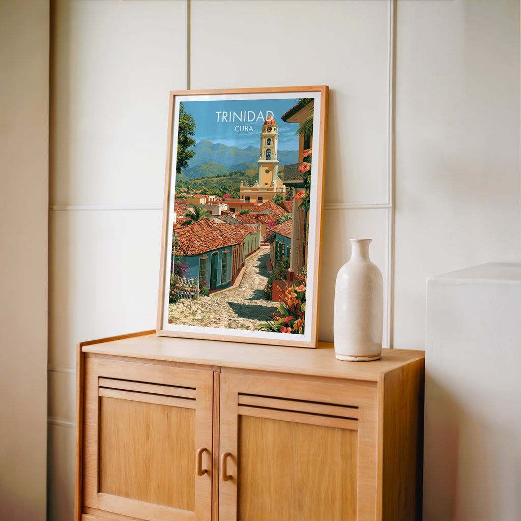 Green mountains behind Trinidad in an oak frame on a light oak cabinet, cream panelled wall, pale bottle vase