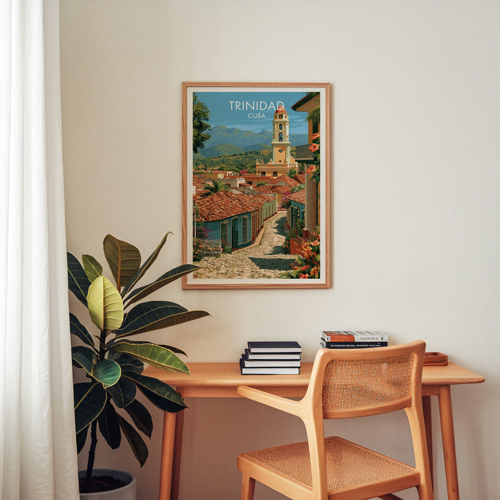 Trinidad street poster in an oak frame above a wooden home-office desk with a cane chair and a rubber plant left