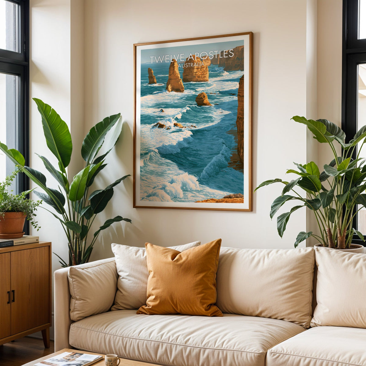 Twelve Apostles travel poster in an oak frame above a cream sofa with a burnt orange cushion and plants
