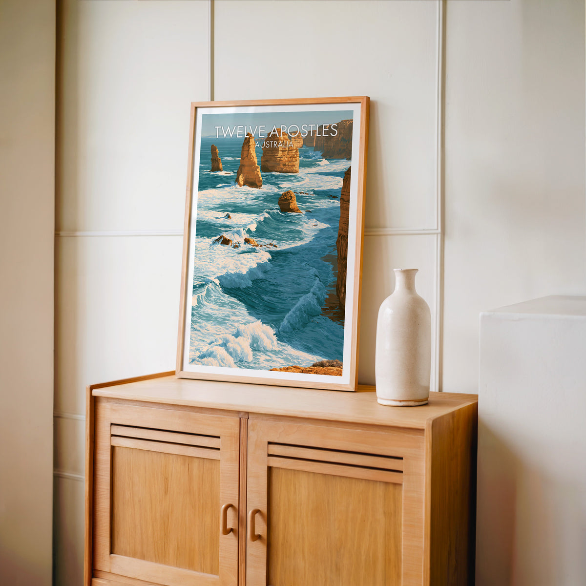 Australian coastline print in an oak frame on a light oak cabinet against a cream panelled wall