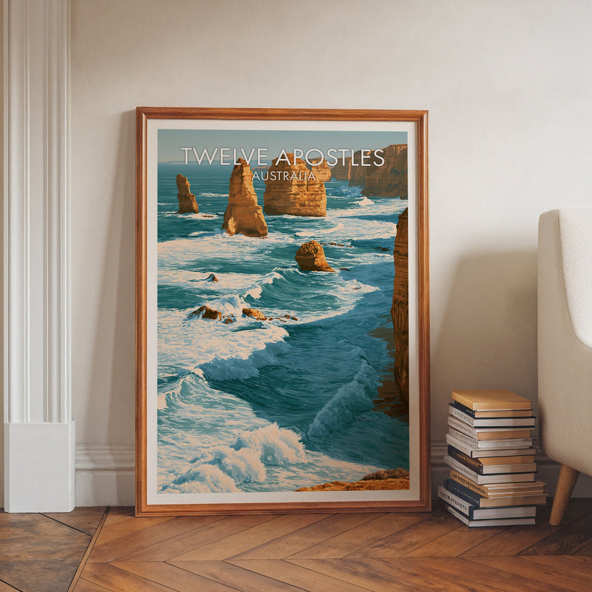Great Ocean Road artwork in a walnut frame on herringbone floor beside book stacks and a pale armchair