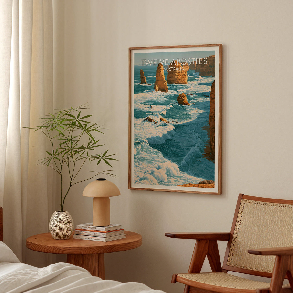 Coastal bedroom print in an oak frame above a round bedside table with a mushroom lamp and bamboo stems