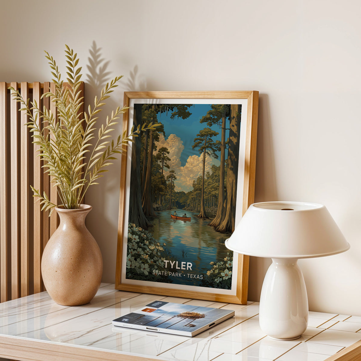 Texas woodland print framed in oak on a balanced stone table with dried stems, a lamp and magazines.