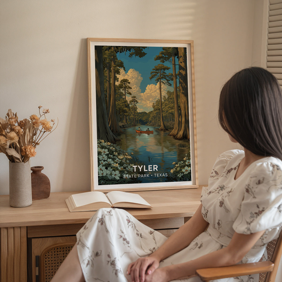 A woman in a white dress sits beside the Tyler State Park print in oak on a sideboard with dried stems.