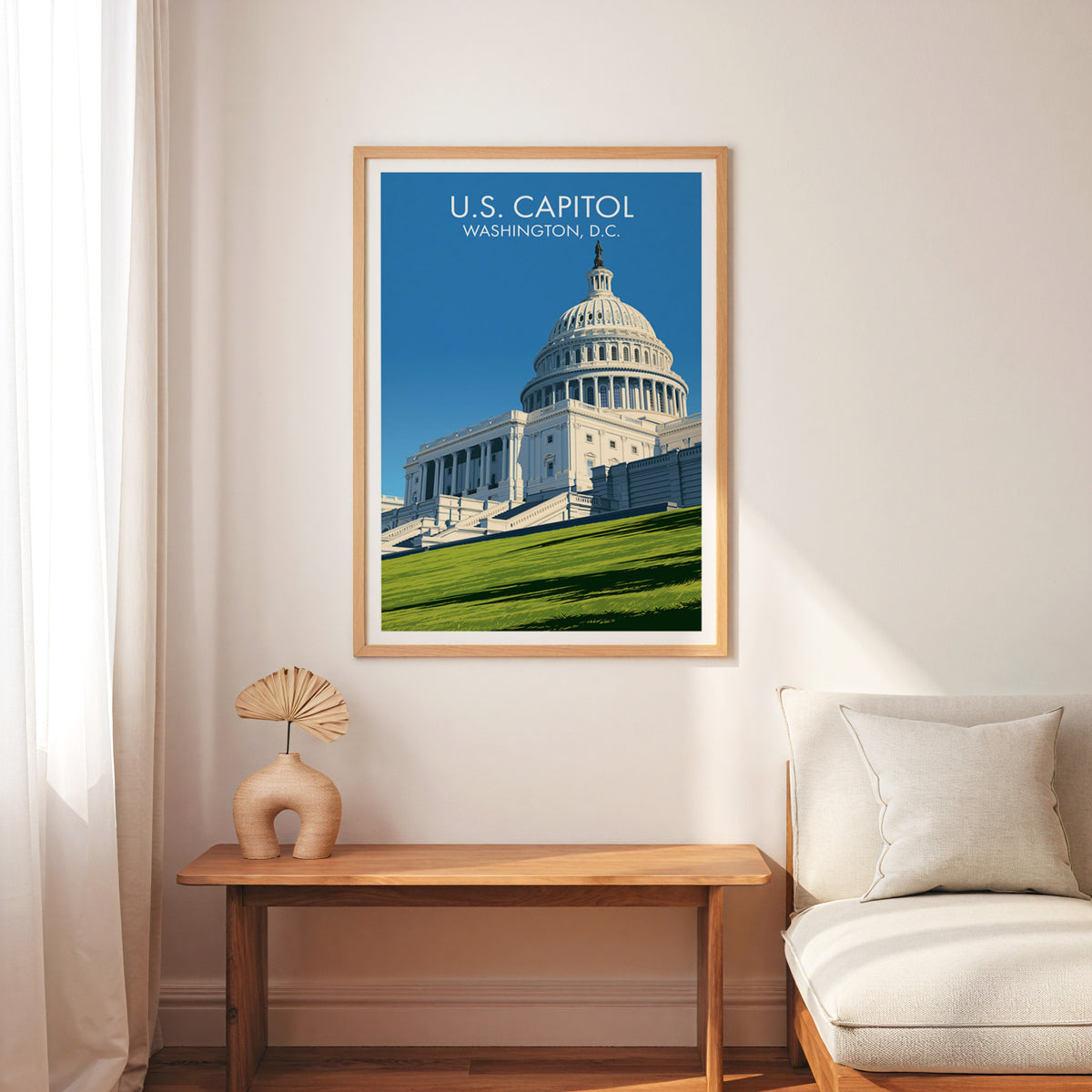 US Capitol art print in an oak frame over a slim wooden bench, cream armchair and a woven palm fan.