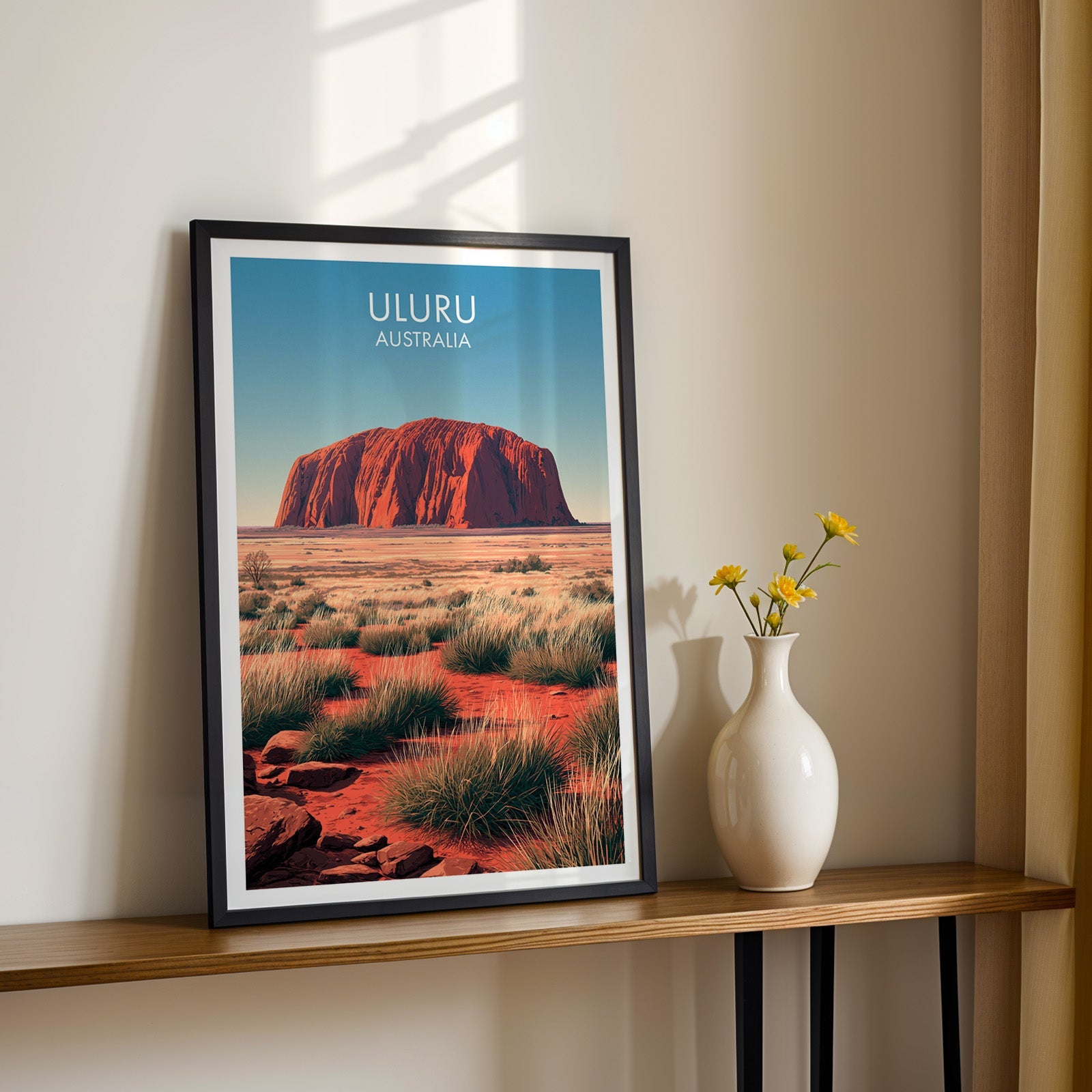 Red centre artwork in a black frame on a wood shelf with yellow daisies on a sunlit cream wall