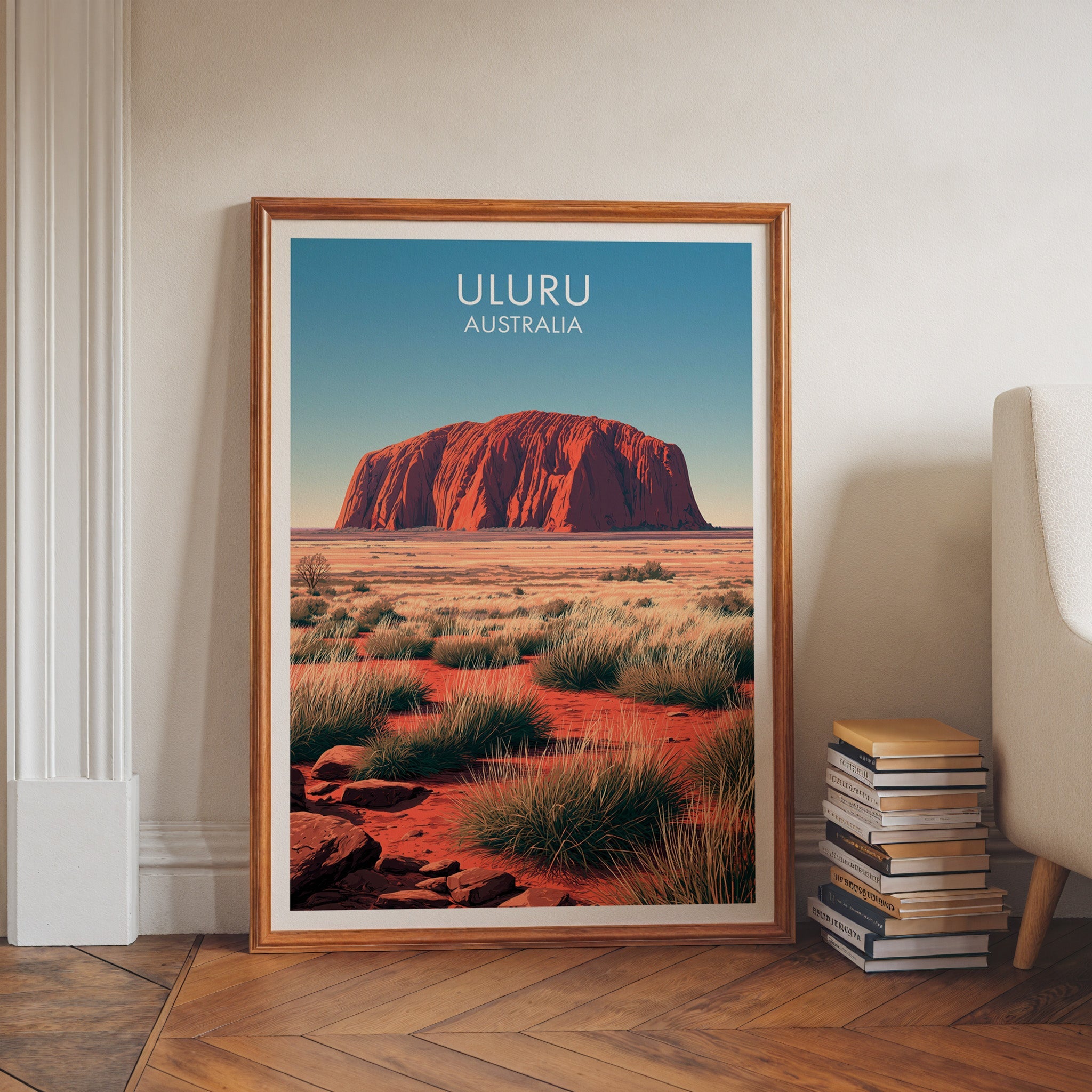 Central Australia poster in a walnut frame on herringbone floor beside book stacks and a pale armchair