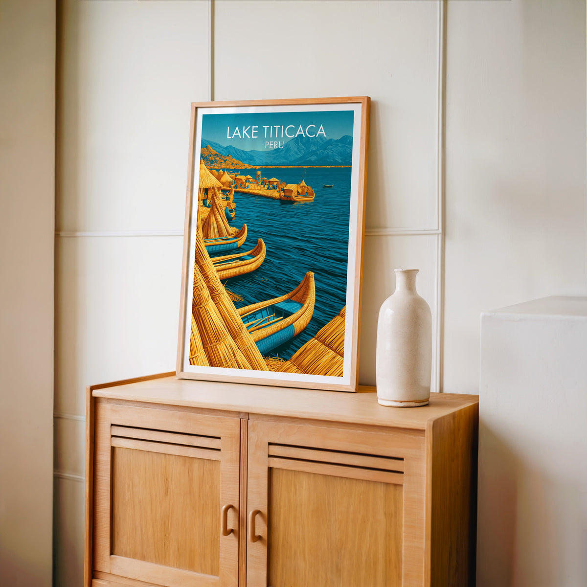 Peru lake village print in an oak frame on a light oak cabinet against cream panelling with a tall vase
