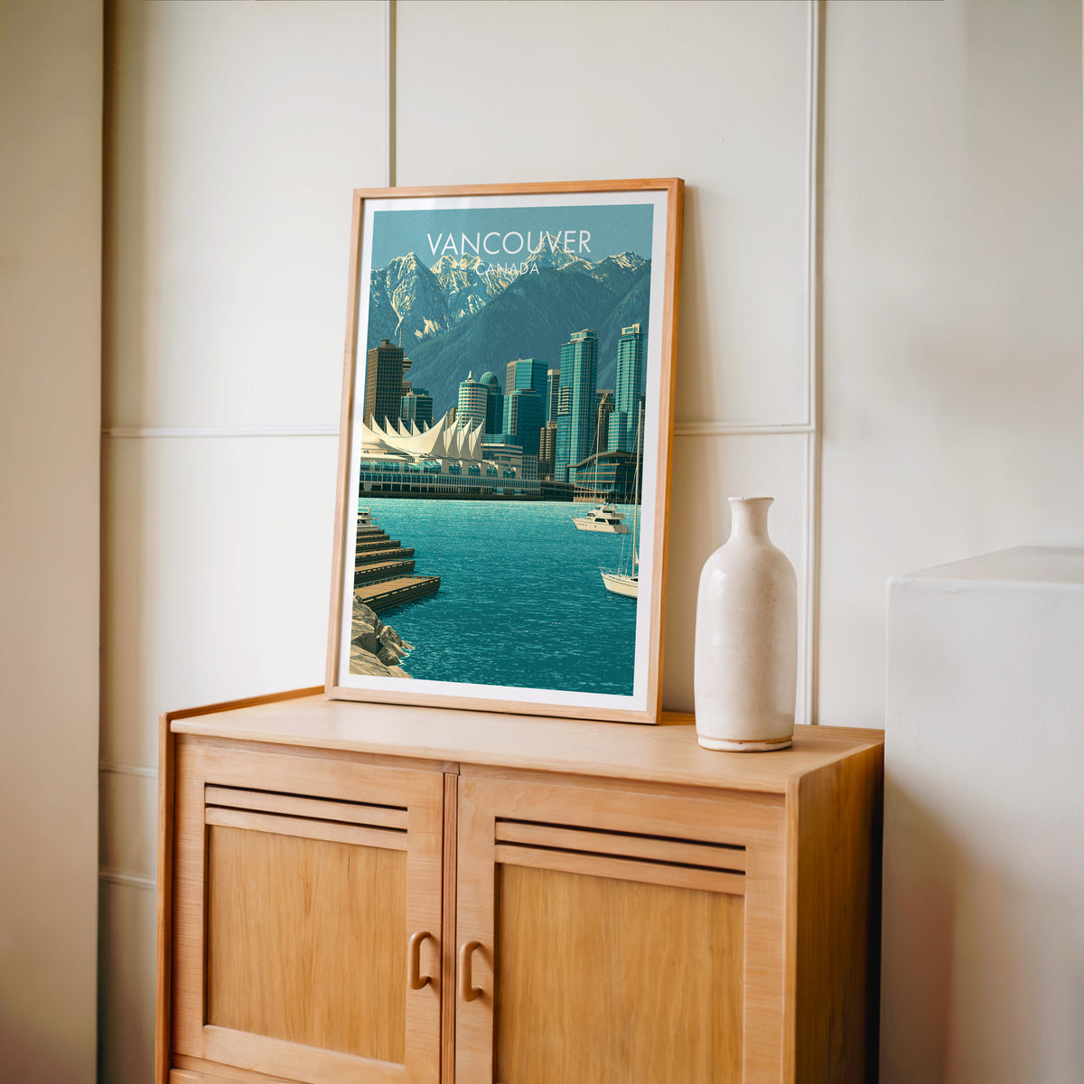 Vancouver North Shore mountains art in an oak frame on a light wood cabinet beside a stoneware vase