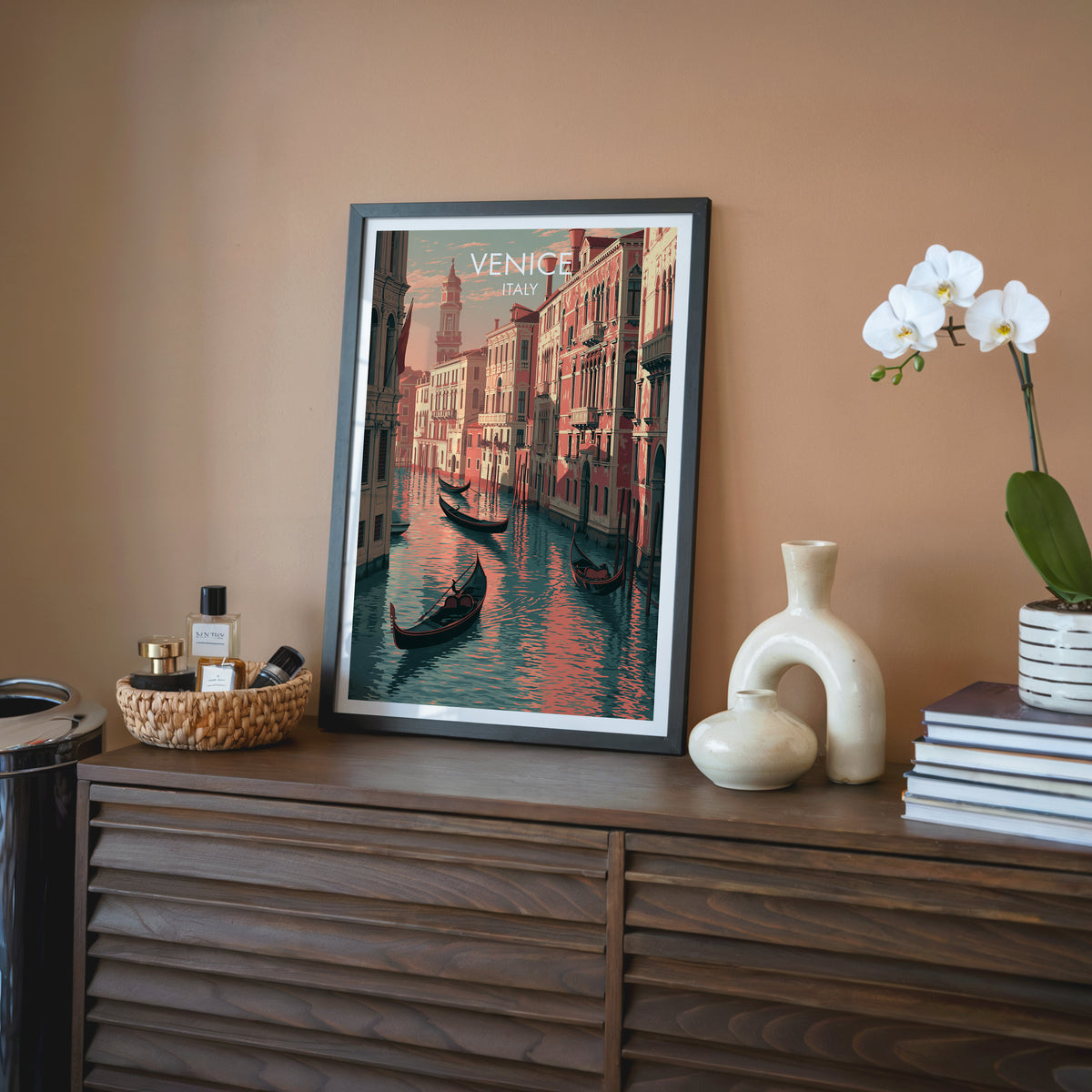 Venice travel wall art in a black frame on a walnut sideboard against a terracotta wall with an orchid