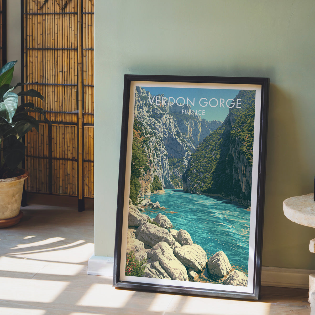 Verdon limestone canyon poster, dark frame leaning on a sage-green wall beside a bamboo screen and a peace lily