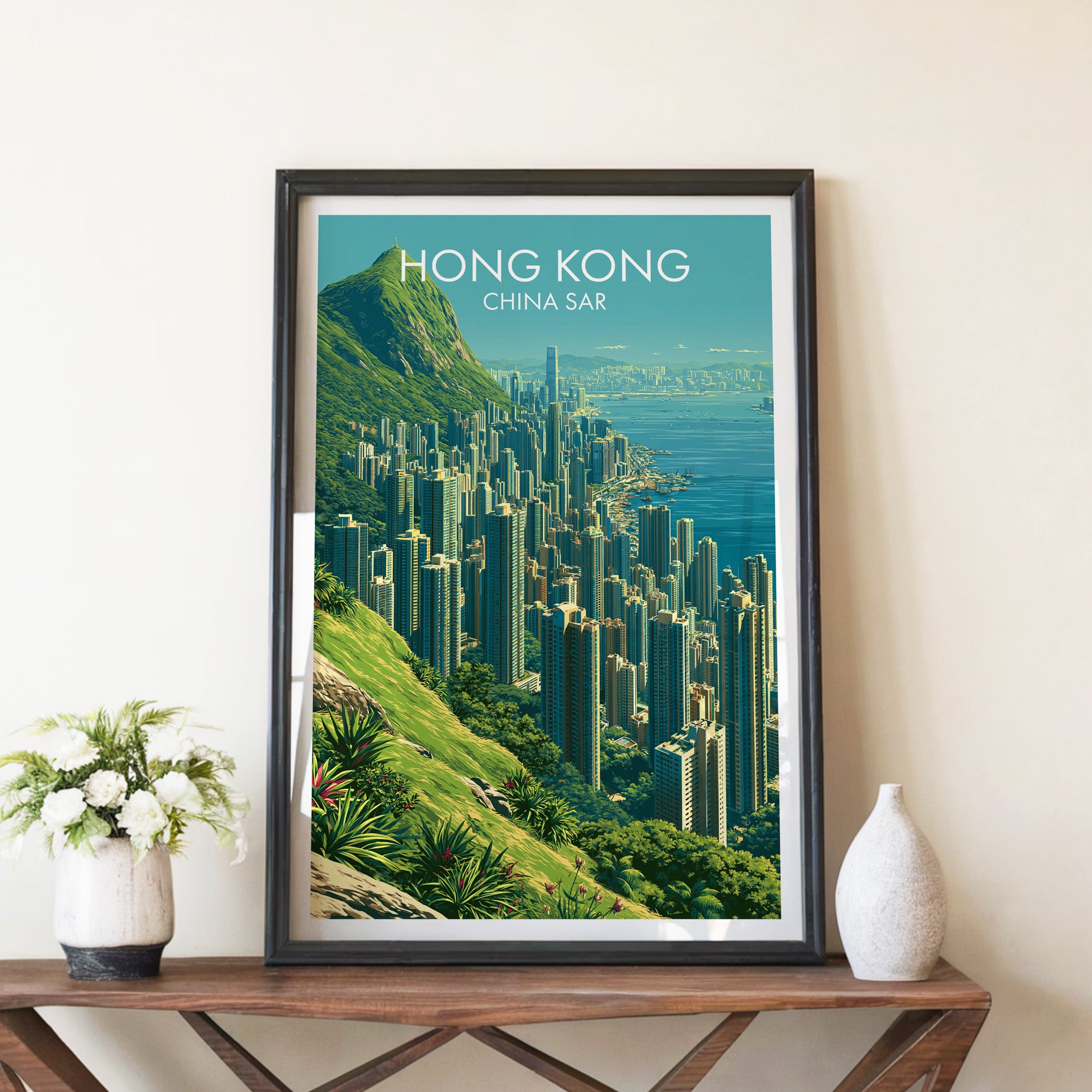Victoria Peak Hong Kong travel poster in a black frame on a wooden console table with white flowers
