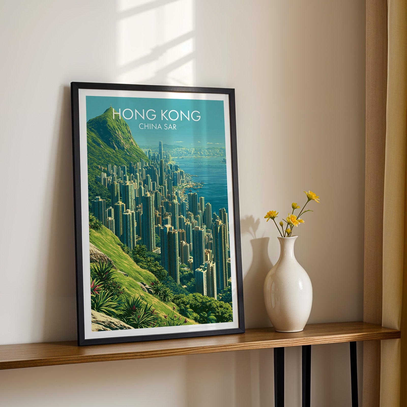Black framed Victoria Peak Hong Kong print on a narrow hallway console in sunlight, styled with yellow flowers