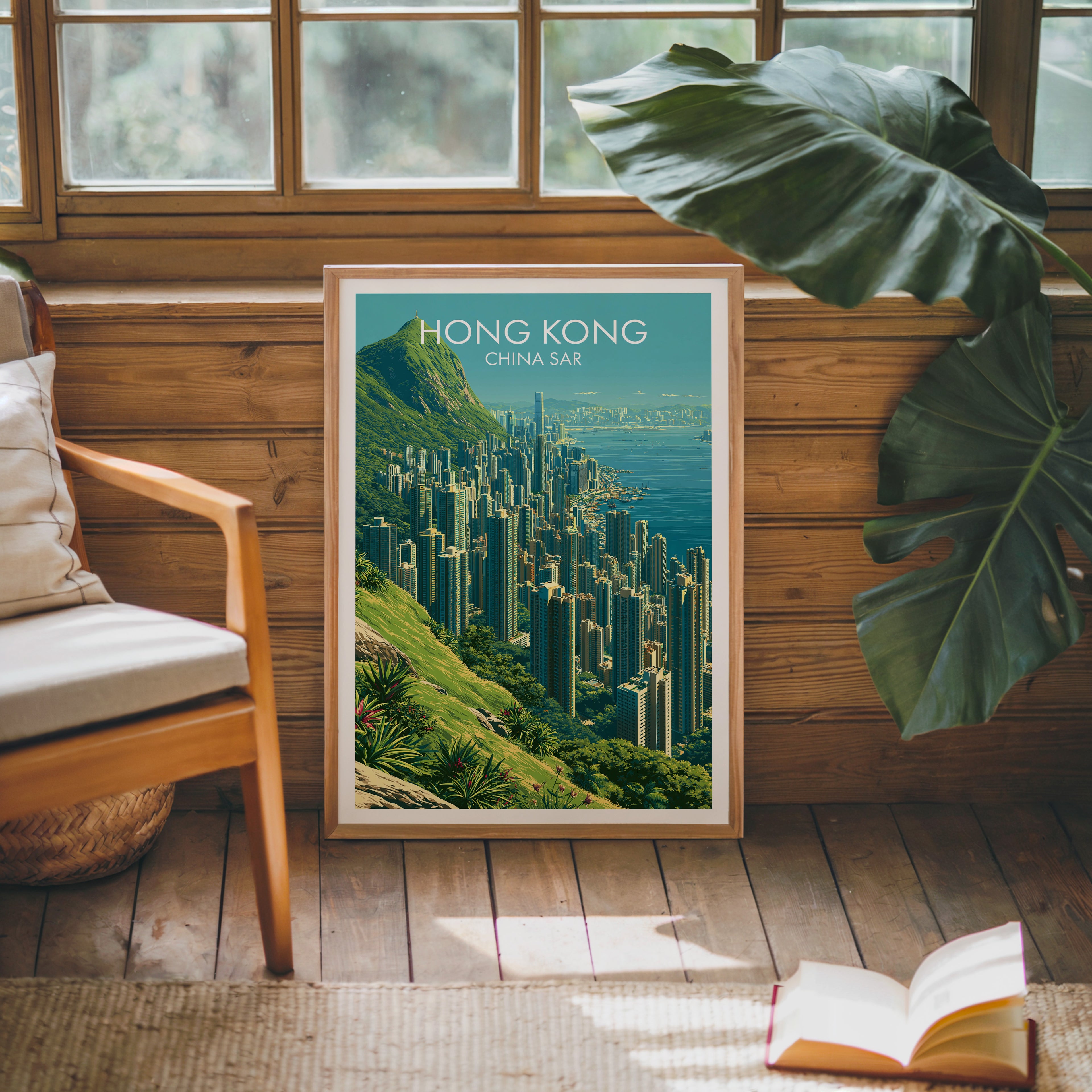 Framed Victoria Peak Hong Kong poster leaning against a timber cabin wall with monstera leaves and an open book