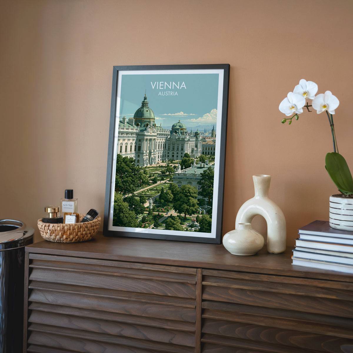 Vienna travel wall art in a black frame on a walnut sideboard against a terracotta wall with an orchid