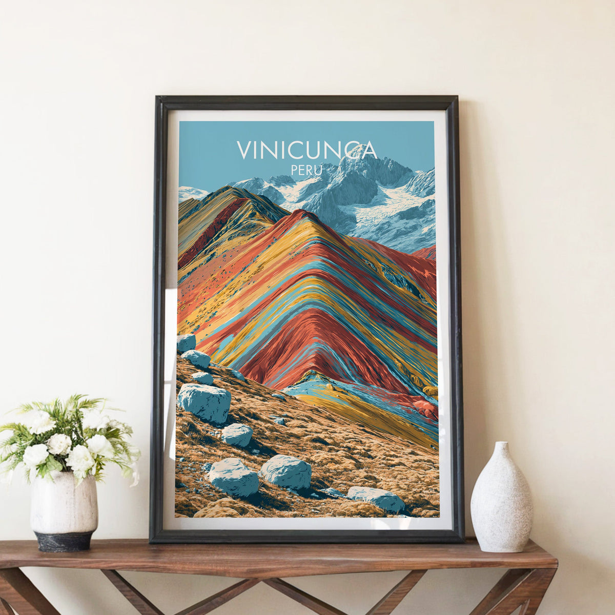 Rainbow Mountain print in a black frame on a brown console table with white flowers in a ceramic vase