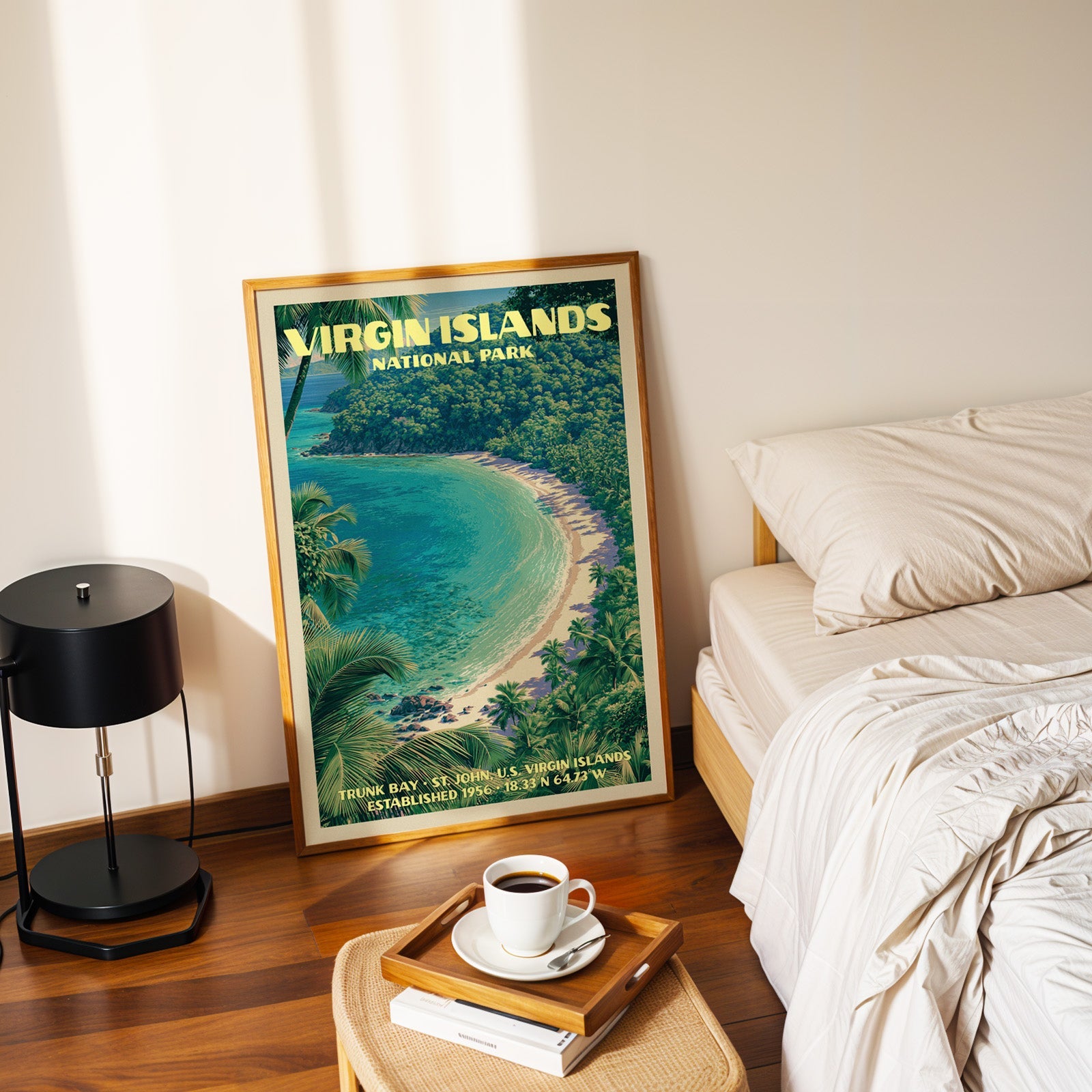Trunk Bay Virgin Islands print in a gold frame on the floor beside a made bed and a black table lamp