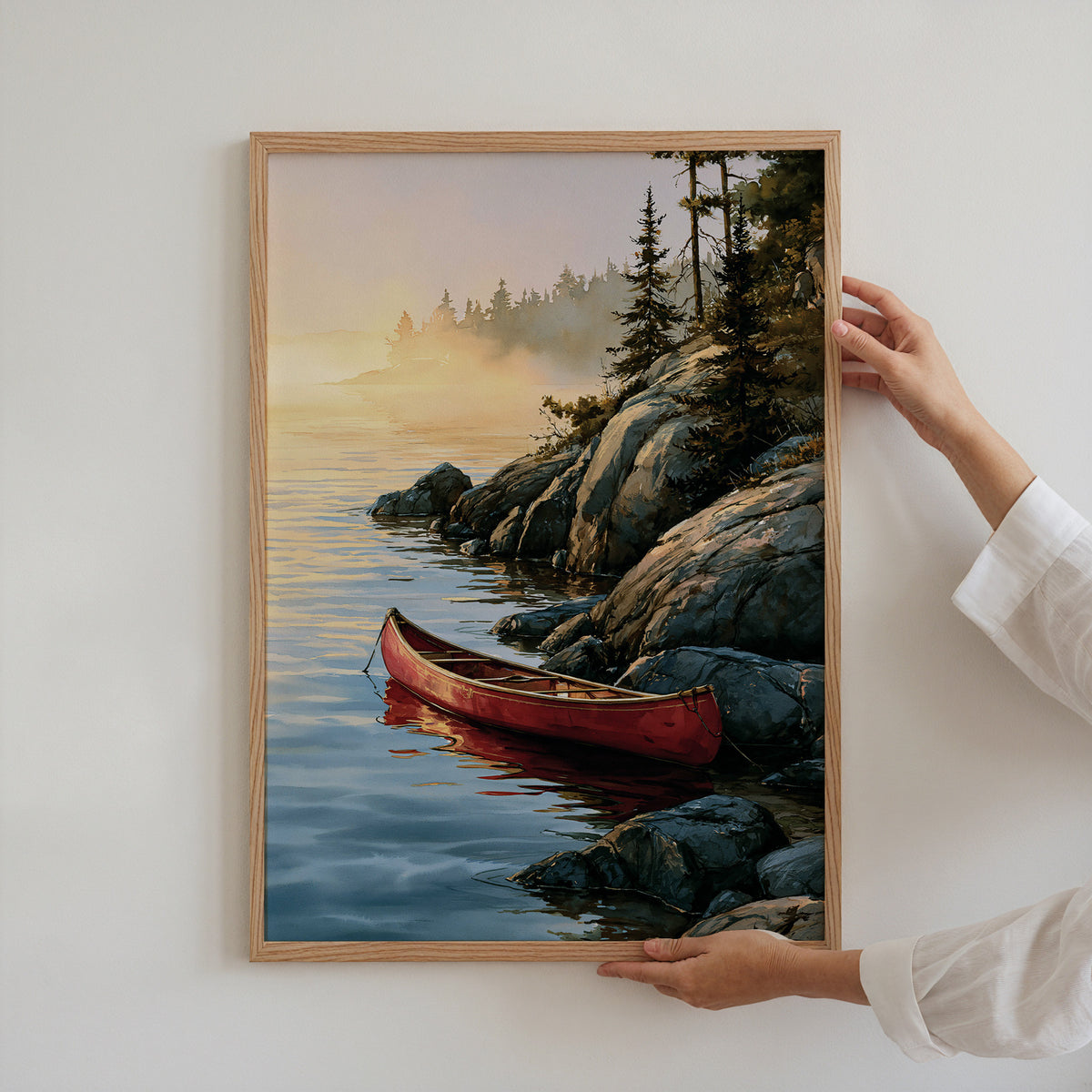 Hands holding an oak-framed Voyageurs National Park watercolor art print against a plain white wall