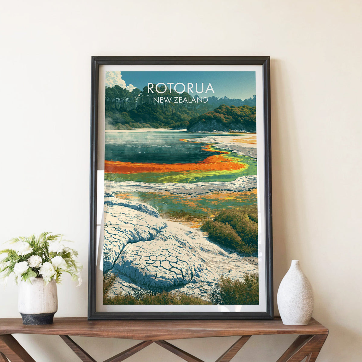 Rotorua geothermal poster in a black frame on a walnut console with white peonies and a stone vase