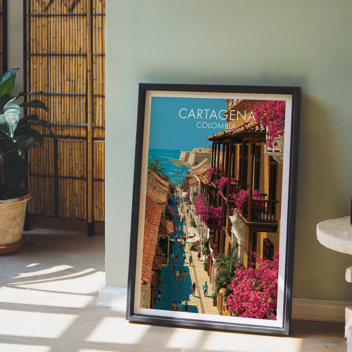 Old town street art in a dark brown frame on pale wood flooring by a sage green wall, bamboo screen and clay pot