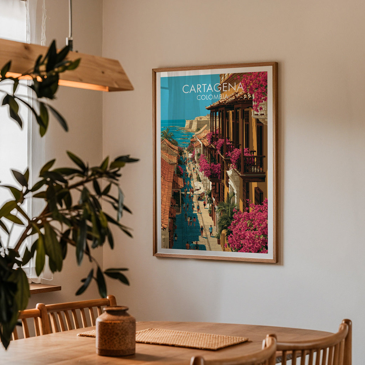 Tiled rooftops and sea art in an oak frame in a dining corner with a wood table, cane chairs and an olive branch