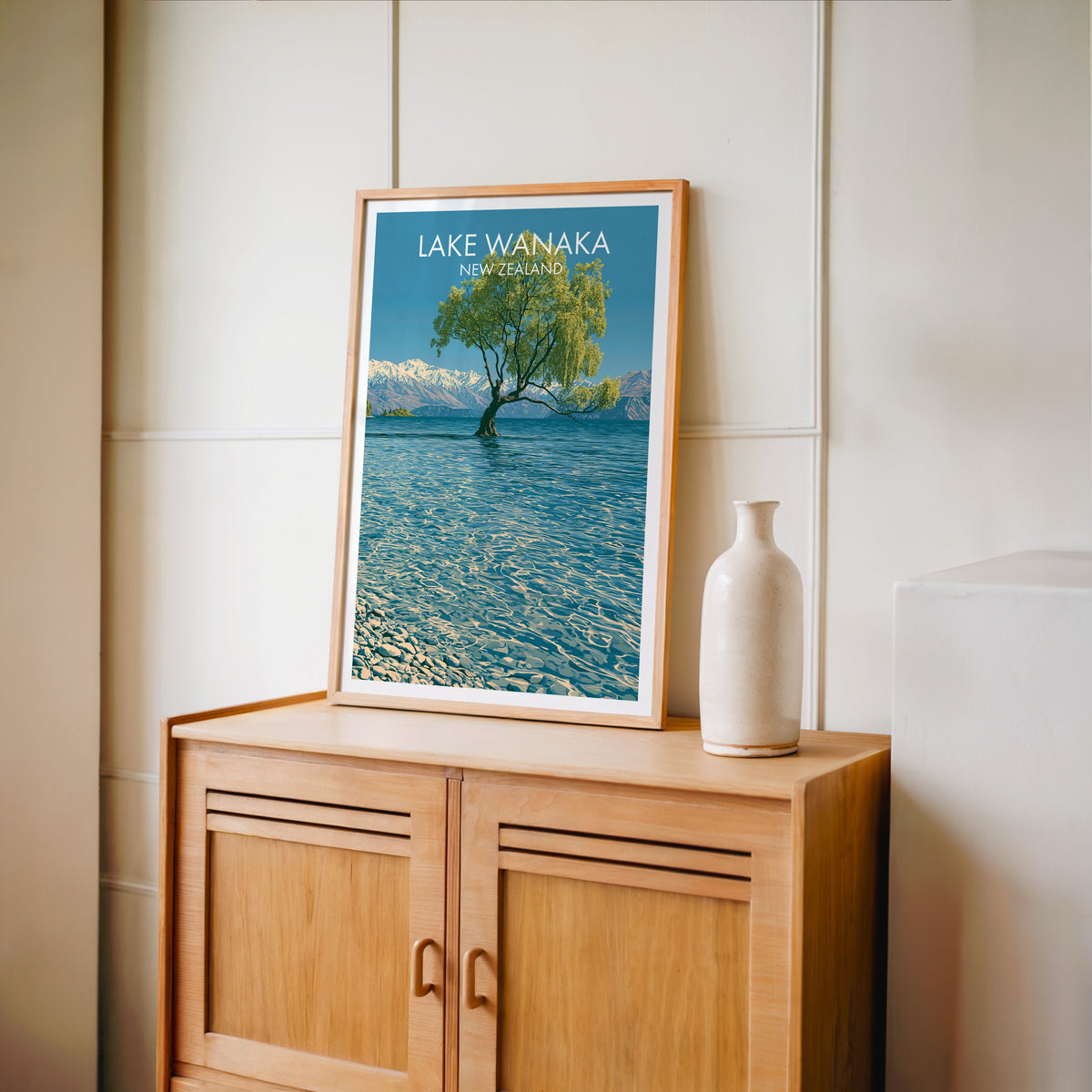 Snowy peaks and lake print in an oak frame on a light oak cabinet against a cream panelled wall