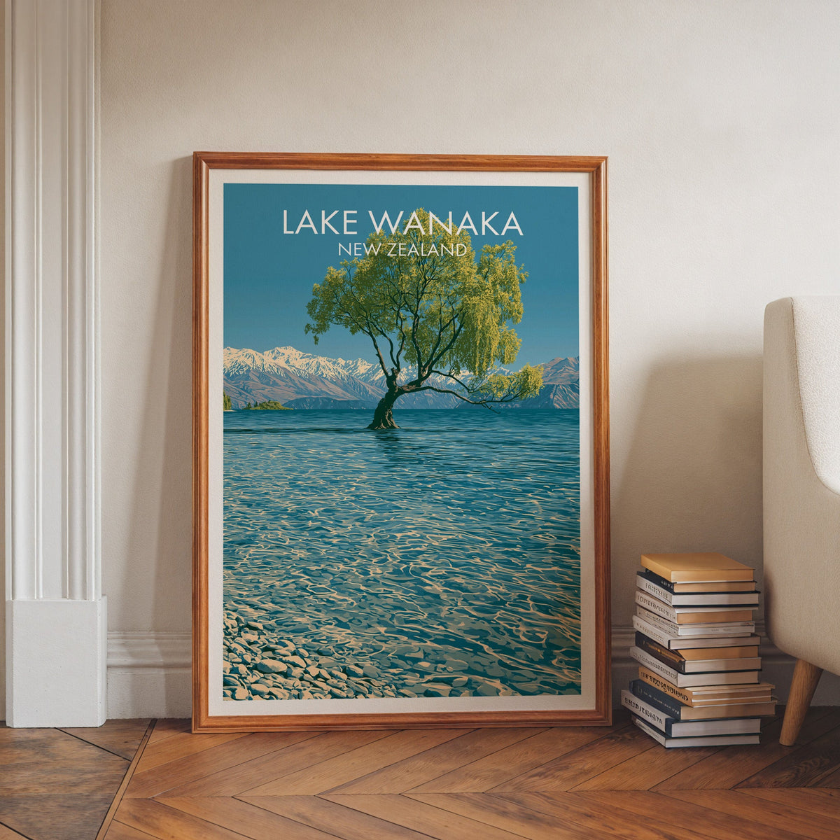 Rippled blue lake artwork in a walnut frame on a herringbone floor beside stacked books and a chair
