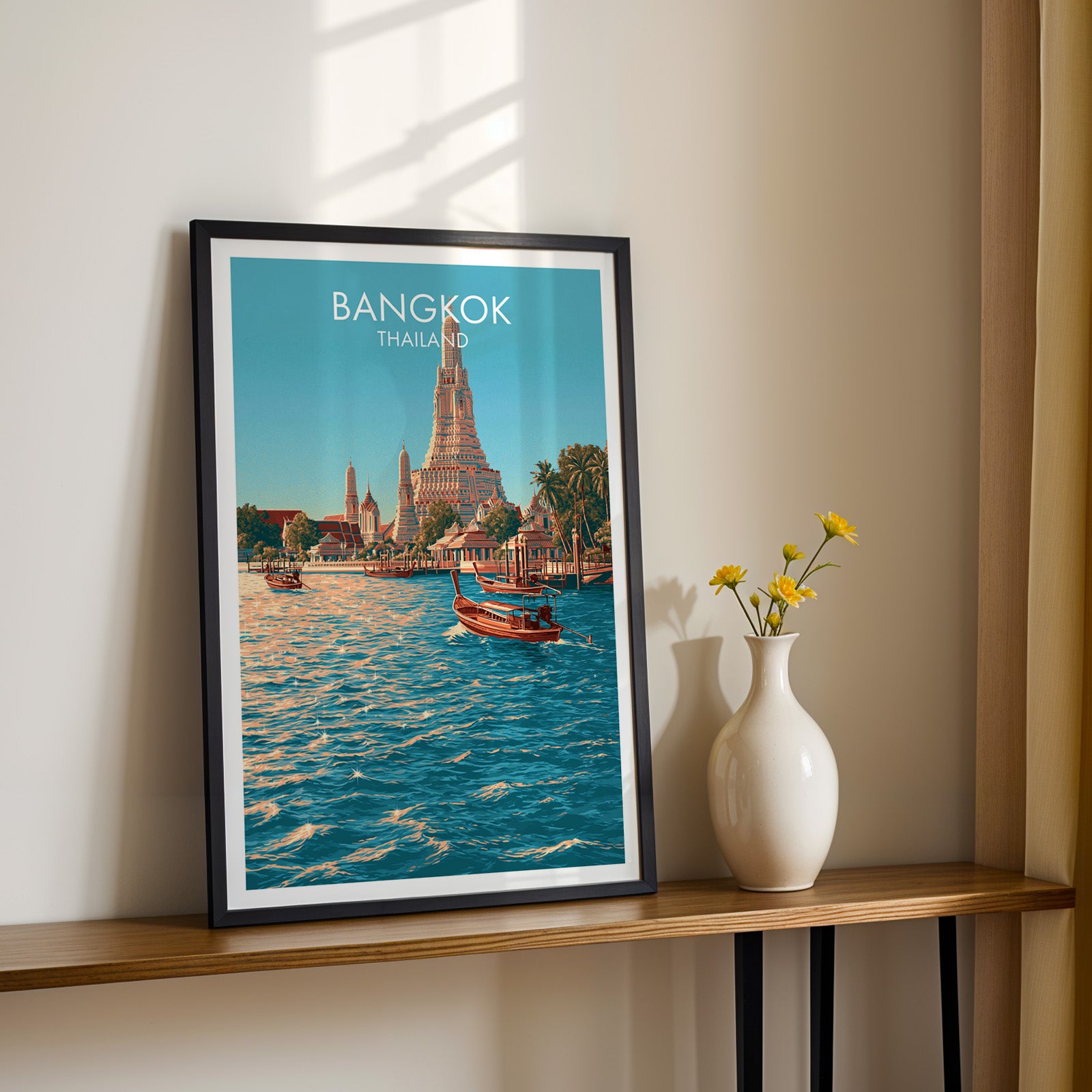 Black framed Wat Arun Bangkok Thailand print on a narrow hallway console in sunlight, styled with yellow flowers